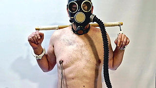 Dominatrix plays with slave's nipples in a gas mask and ties his balls with rope